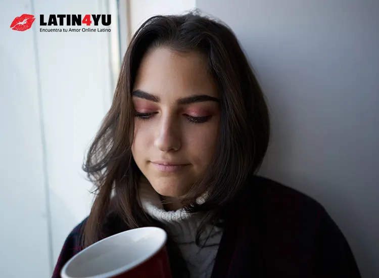 Mujer triste cerca de la ventana con taza roja y cuadros